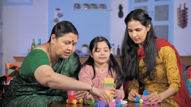 Pretty Indian girl playing indoor games with her mother and grandmother - Quarantine life. Three generation women playing with blocks during their free time - leisure and relaxation
