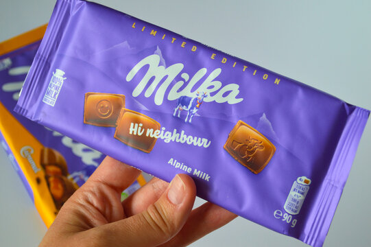 Hand holding a purple Milka alpine milk chocolate bar package with limited edition design in a bright studio environment.
