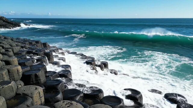 Powerful ocean waves crashing against hexagonal basalt columns on a sunny day at the Giant's Causeway