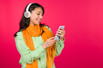 Naklejka premium Young woman smiling enjoying music looking smartphone