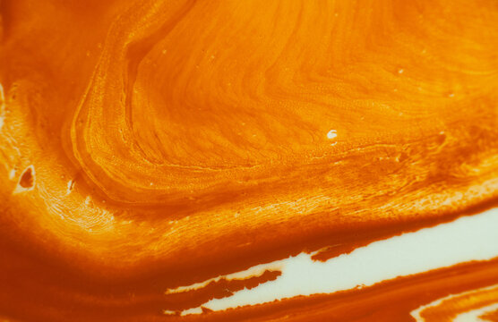 Design of orange and white patterns in fluid art on a canvas in a studio setting