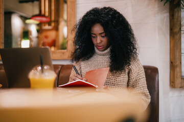 Naklejka na ściany i meble Talented Black writer writing notebook research project planning checklist. Creative African American student studying online freelance remote office workspace, real people equity inclusion