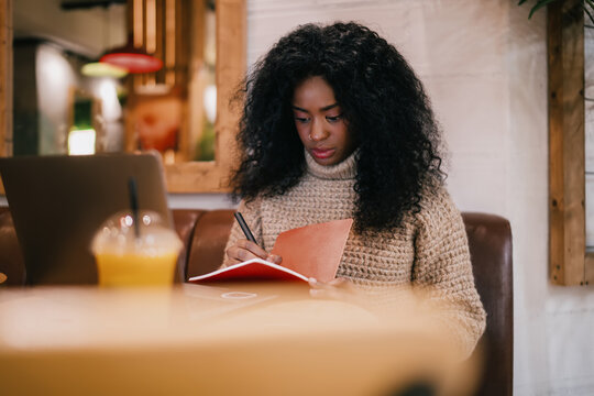 Talented Black writer writing notebook research project planning checklist. Creative African American student studying online freelance remote office workspace, real people equity inclusion