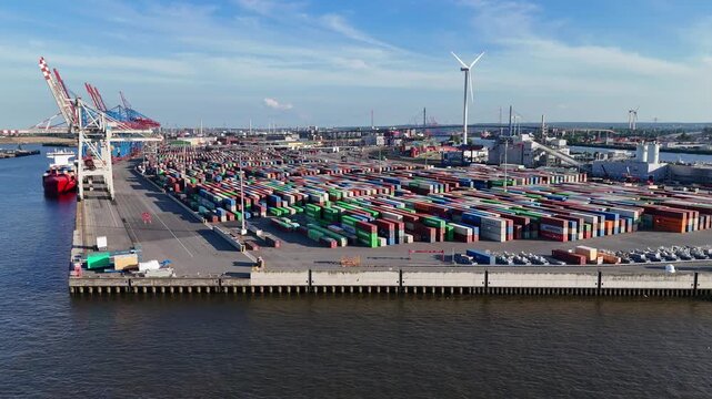 Hamburg, Germany - 01 June 2026: Aerial view of HHLA Container Terminal Tollerort with rows of colorful shipping containers, gantry cranes and a wind turbine under a clear sky.