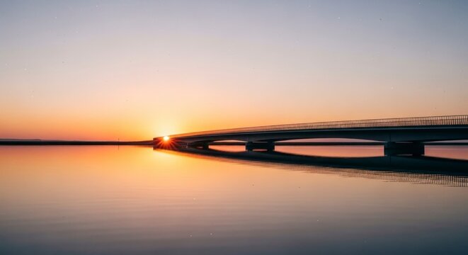 Silhueta tranquila de uma ponte sobre a &aacute;gua ao p&ocirc;r do sol, com um c&eacute;u alaranjado vibrante.