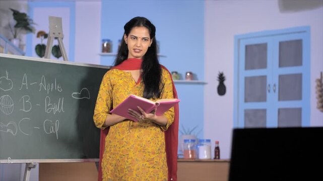 Young woman teacher teaching children online - e-learning classes during Covid pandemic. Attractive academic instructor standing in front of a board taking lessons on a conference call - remote lea...