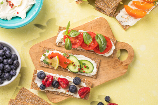 Fresh crunchy rye crispbreads with different toppings on green table, top view