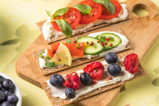 Fresh crunchy rye crispbreads with different toppings on green table, top view