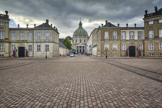Copenhagen, Denmark - 01 June 2026: View of Amalienborg Palace square with the green dome of Frederik's Church in the background under a cloudy sky.