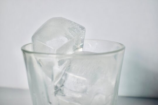 Macro shot of a clear frozen ice block with tiny trapped air bubbles inside a glass cup, showcasing detailed texture and a bright, fresh atmosphere.