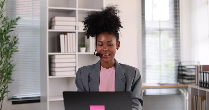 African american businesswoman smiling, wearing a headset with a microphone, providing online assistance and support while working from her home office setup