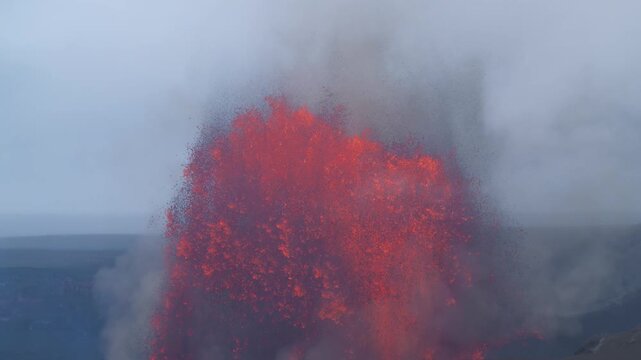 View of Halemauma'u Crater erupting with glowing red lava fountains and thick volcanic smoke in Hawaii County, Hawaii, United States.