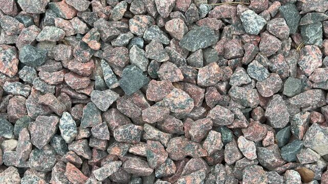 Close-up medium rubble gravel in daylight, dense spread of angular crushed stones with pink and gray tones, tight composition