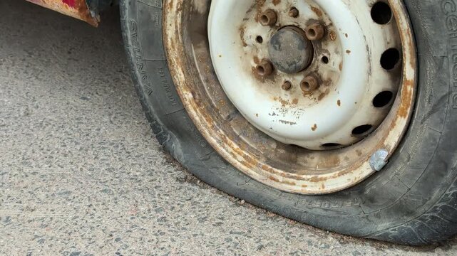 Close-up rusted rim with flat tire on asphalt road during daytime, deflated rubber bead pressed against corroded steel wheel