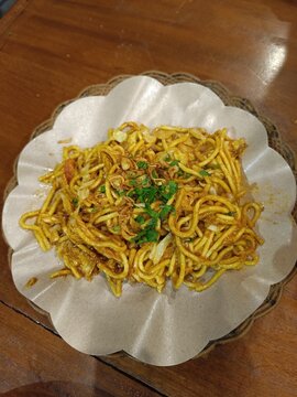 Delicious Indonesian bakmi goreng or fried noodles topped with fried shallots and celery. Authentic Asian street food flat lay on a rustic wooden background, perfect for menus.