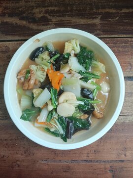 Delicious capcay or Indonesian stir-fried mixed vegetables with meatballs served in a white bowl. Healthy Asian culinary flat lay on a rustic wooden background for menus.