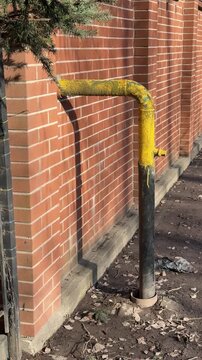 Yellow gas pipe through brick wall showing residential supply to cottage village, metal support post and iron fence, evergreen