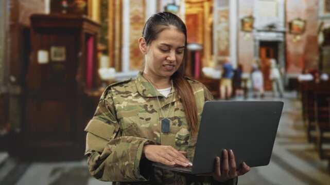 Woman soldier in camouflage uniform typing on laptop with fingers, dog tags visible, smiling inside ornate building; pride duty service.