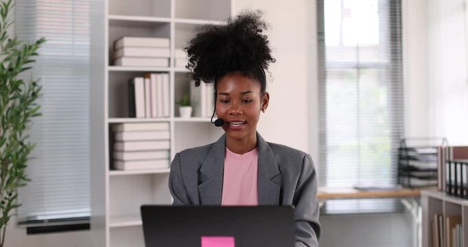 African american businesswoman smiling, wearing a headset with a microphone, providing online assistance and support while working from her home office setup