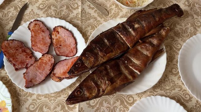 Smoked walleye and pork steaks plated on white plate with patterned tablecloth, golden crispy skin, sliced pork rounds