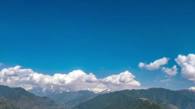 View of the majestic mountain range with green slopes and snow-capped peaks under a bright blue sky with fluffy white clouds in Naran, Khyber Pakhtunkhwa, Pakistan.