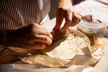 Fototapeta premium Hands preparing tacos at home, filling and rolling tortillas to make Golden Beef Tacos, also called Flautas de res, a typical Mexican dish.