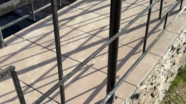 Porch entrance with new tiles, sunlit concrete steps and black metal railing casting long shadows, textured masonry riser