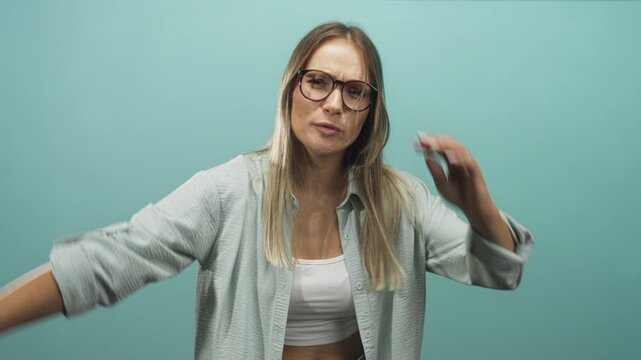 Woman extends arm and gestures with hand while wearing glasses in studio, casual shirt and visible midriff; frustration reflection.