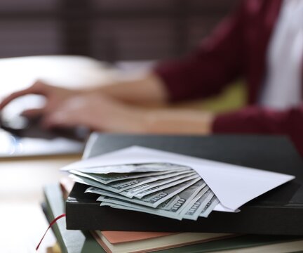 Woman working with laptop at table indoors, focus on envelope, money and notebooks