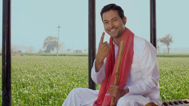A happy farmer showing his ink-marked finger and his belief in the right to vote. A medium shot of a modern Indian peasant showing his ink-marked index finger after casting a vote - Right To Vote C...