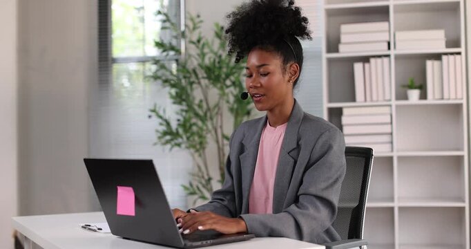 African american businesswoman smiling, wearing a headset with a microphone, providing online assistance and support while working from her home office setup