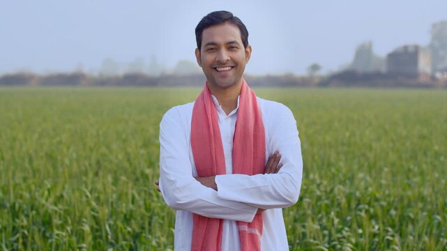 Young attractive farmer happily standing in his field while folding his hands. Medium shot of an Indian boy wearing kurta pajama and safa standing in his village farm