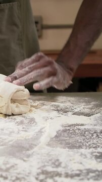 Vertical video: Shaping green-aproned baker folding dough from rolled log on floured counter, watch