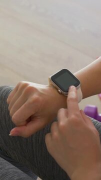 Vertical video: Tapping wrist with bangle, swiping dark smartwatch to wake in grey leggings at home