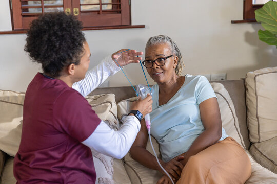 Senior African American woman getting nebulizer on sofa as aide in scrubs holding mask, copy space