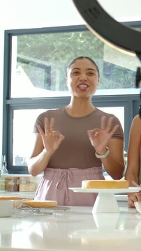 Vertical video: On cue woman in brown top gesturing, demoing cake at kitchen island with ring light