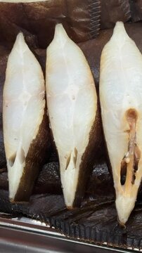 Cold smoked halibut steaks on counter, close-up of glistening white flesh and brown skin on chilled tray, market display suggests