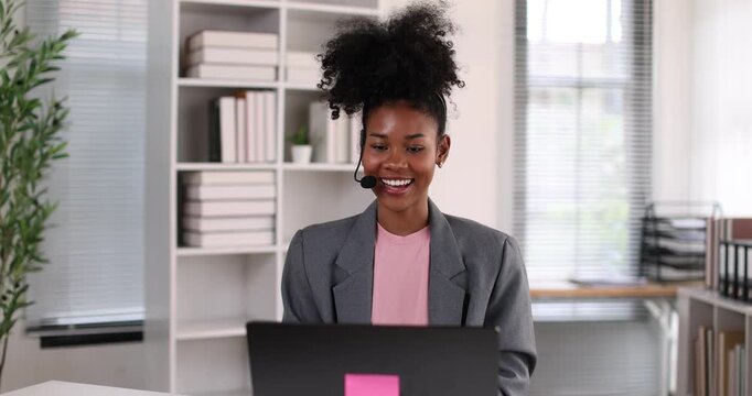 African american businesswoman smiling, wearing a headset with a microphone, providing online assistance and support while working from her home office setup