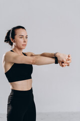 Fototapeta premium Athletic woman in sportswear stretching arms and wrists before fitness training against light studio background