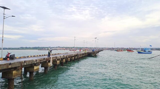 PAMEKASAN, INDONESIA - JANUARY 10, 2026: Traditional fisherman throwing a casting net into the sea from a concrete pier in Madura, Indonesia. This cinematic footage captures the skillful technique.