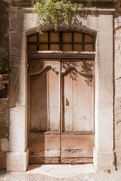 Weathered wooden doors frame a rustic stone archway, Biot
