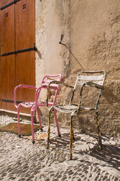 Rusted chairs lean against a sunlit stone wall