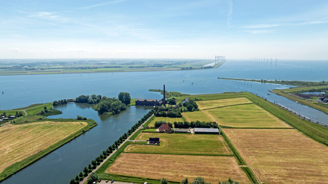 Aerial view of the historic Ir. D.F. Woudagemaal pumping station surrounded by green fields and the IJsselmeer coast in Lemmer, Friesland, Netherlands.