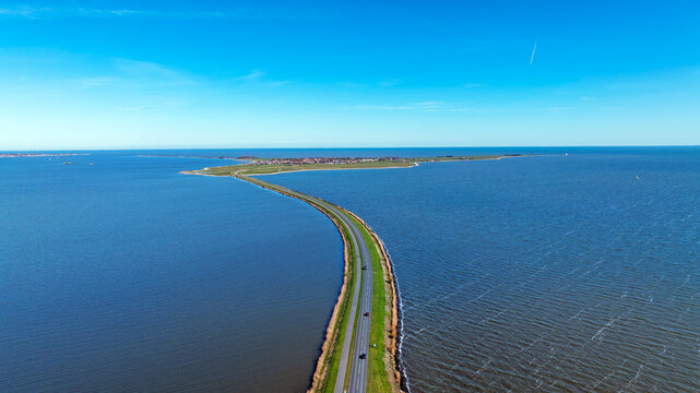 Aerial view of the long causeway road leading to the historic village of Marken across the blue waters of the Markermeer under a clear sky in Marken, North Holland, Netherlands.