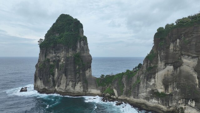 Aerial view of the towering rock formation at Pantai Pangasan with lush greenery and steep cliffs overlooking the ocean Kecamatan Kebonagung, Jawa Timur, Indonesia.