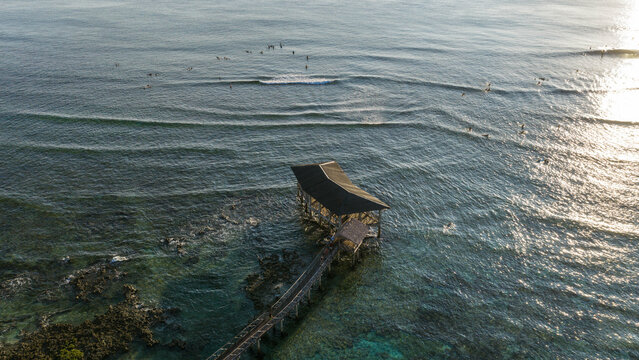 Aerial view of Cloud 9 Surfing Area with surfers catching waves near the iconic wooden pier over clear turquoise water in General Luna, Caraga, Philippines.