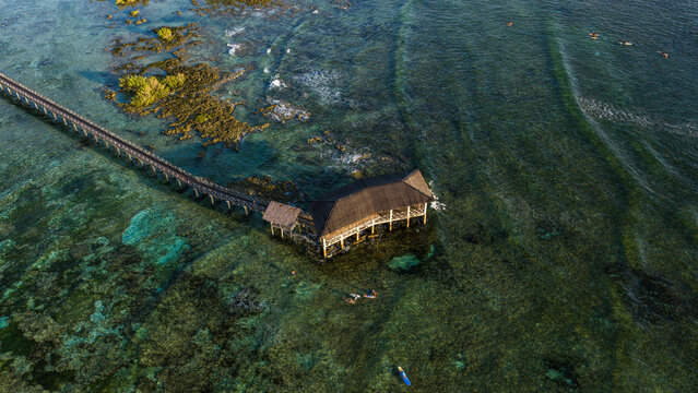Aerial view of the Cloud 9 Surfing Area featuring a long wooden boardwalk and pavilion over vibrant coral reefs and turquoise water in General Luna, Caraga, Philippines.