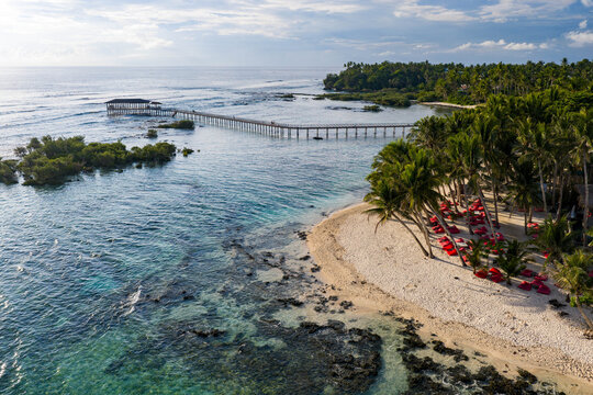 Aerial view of the Cloud 9 Surfing Area featuring a long wooden boardwalk over turquoise water and a palm-fringed beach with red bean bags in General Luna, Caraga, Philippines.