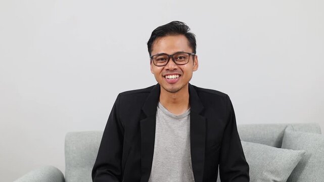 Man smiling and waving at camera during a virtual video conference, friendly businessman greeting colleagues from a modern office, webcam headshot for remote work communication