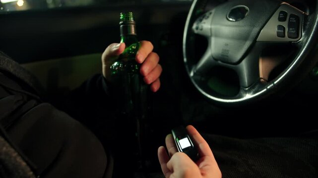 Adult drunk caucasian man conduct sober test at night. Night scene with man holding breath device and green bottle with alcohol. Interior night setting of using handheld breath analyzer in car
